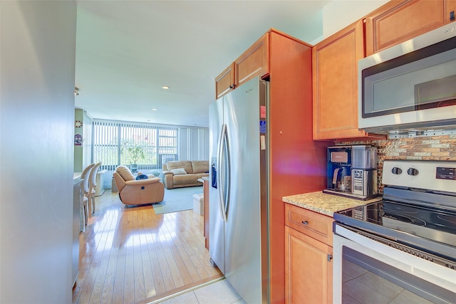 10-11 162nd St Unit 7A, Beechhurst, NY 11357 - kitchen with appliances with stainless steel finishes, open floor plan, decorative backsplash, light stone counters, and light wood-style flooring