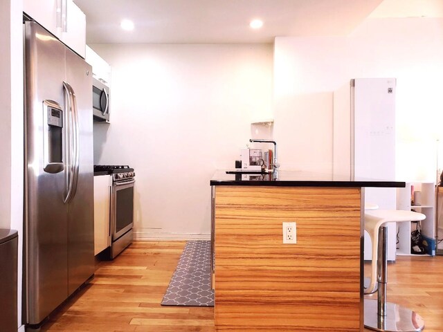2311 21st Ave Unit 3C, Astoria, NY 11105 - kitchen featuring stainless steel appliances, light wood-style flooring, dark countertops, white cabinets, and recessed lighting