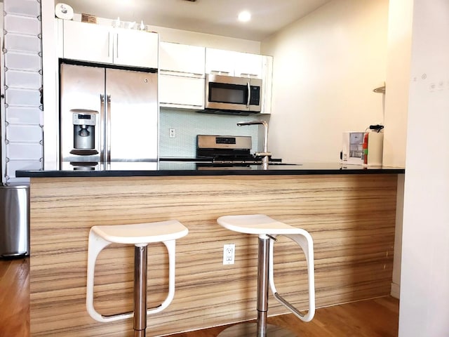 2311 21st Ave Unit 3C, Astoria, NY 11105 - kitchen with appliances with stainless steel finishes, a kitchen bar, wood finished floors, white cabinetry, and tasteful backsplash