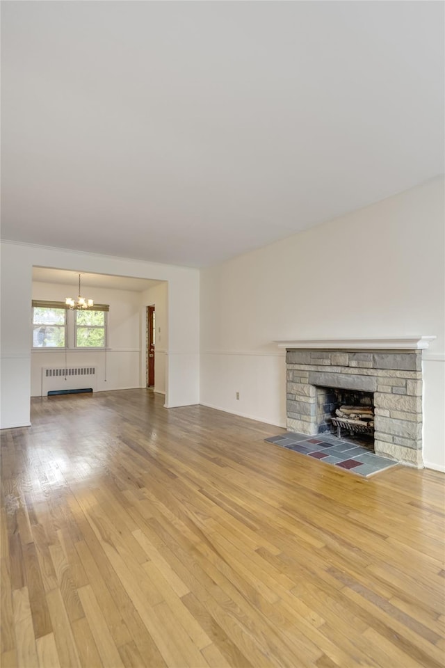 29 Newmarket Rd, Syosset, NY 11791 - unfurnished living room with radiator heating unit, a chandelier, a stone fireplace, and hardwood / wood-style flooring