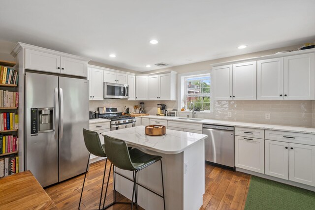63 Liberty St, Beacon, NY 12508 - kitchen with appliances with stainless steel finishes, a sink, hardwood / wood-style flooring, white cabinetry, and a breakfast bar