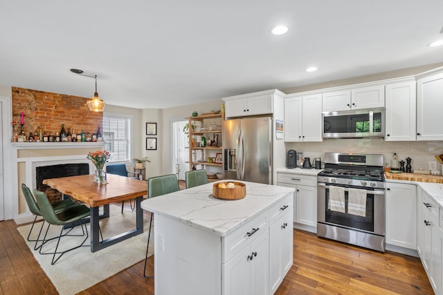 63 Liberty St, Beacon, NY 12508 - kitchen featuring stainless steel appliances, light wood finished floors, white cabinets, a kitchen island, and light stone counters