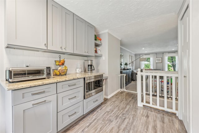 7 Washington Mews Unit 7, Port Chester, NY 10573 - kitchen featuring stainless steel microwave, ornamental molding, decorative backsplash, light wood-style floors, and light stone countertops