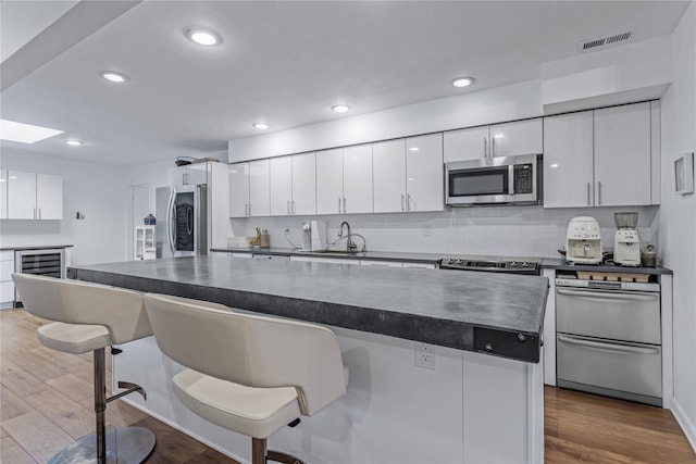 291 Starling Ct, Manhasset, NY 11030 - kitchen featuring appliances with stainless steel finishes, wine cooler, dark countertops, a breakfast bar area, and white cabinetry