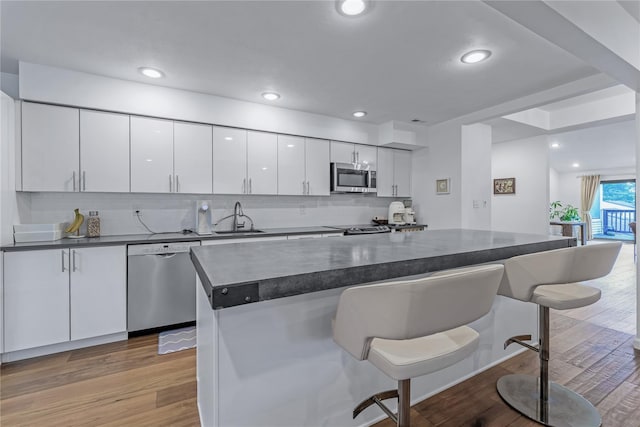 291 Starling Ct, Manhasset, NY 11030 - kitchen featuring stainless steel appliances, dark countertops, a kitchen bar, white cabinets, and light wood-style floors