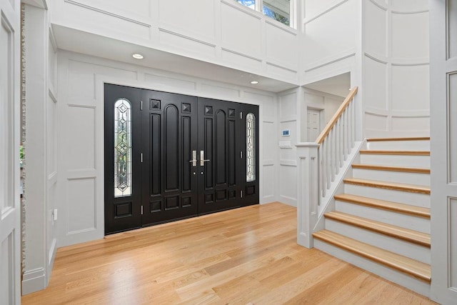 2 Field Ln, Roslyn Heights, NY 11577 - entryway with a decorative wall, stairs, light wood-type flooring, a towering ceiling, and healthy amount of natural light