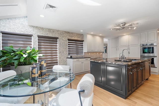 2 Field Ln, Roslyn Heights, NY 11577 - kitchen with stainless steel double oven, a sink, light wood-type flooring, a kitchen island with sink, and dark stone countertops