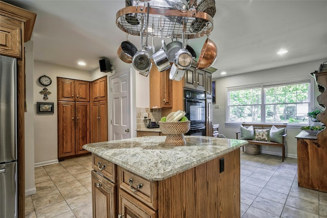 28 Valley Rd, Manhasset, NY 11030 - kitchen featuring freestanding refrigerator, brown cabinetry, light stone countertops, a center island, and baseboards