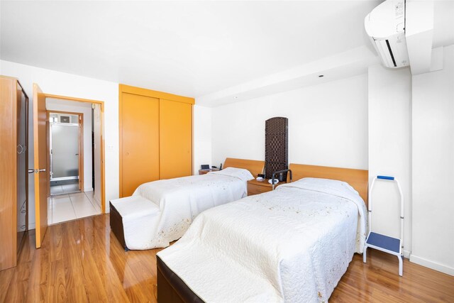 215 Park Row Unit 8B, New York Manhattan, NY 10038 - bedroom with an AC wall unit, light wood-style flooring, a closet, and baseboards