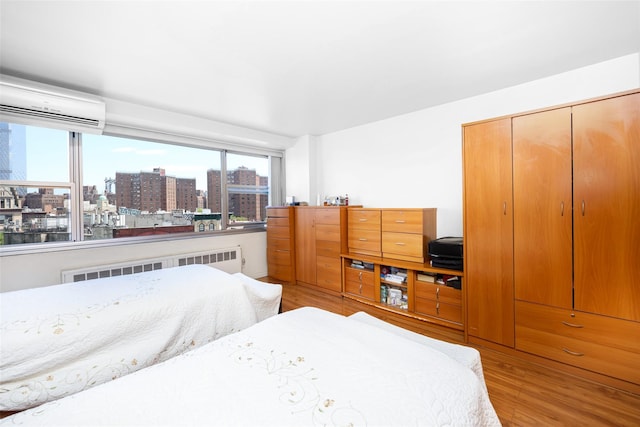 215 Park Row Unit 8B, New York Manhattan, NY 10038 - bedroom featuring an AC wall unit, radiator, light wood-type flooring, a city view, and a closet