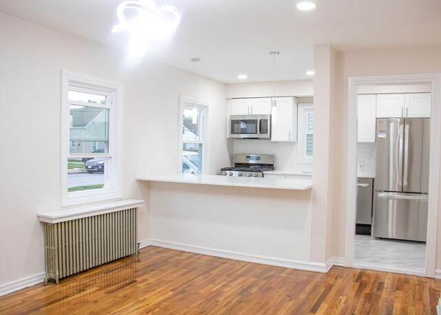 11 Shine Pl, Valley Stream, NY 11581 - kitchen with stainless steel appliances, radiator heating unit, wood finished floors, white cabinetry, and tasteful backsplash