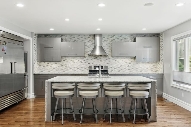 1 Berkley Ct, Briarcliff Manor, NY 10510 - kitchen featuring gray cabinets, wall chimney range hood, built in refrigerator, an island with sink, and decorative backsplash
