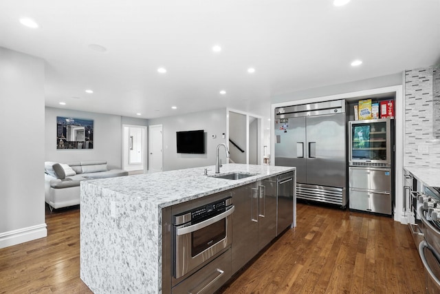 1 Berkley Ct, Briarcliff Manor, NY 10510 - kitchen featuring appliances with stainless steel finishes, a sink, dark wood finished floors, an island with sink, and light stone counters