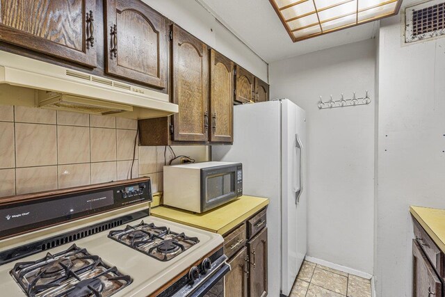 152-18 Union Tpke Unit 4G, Flushing, NY 11367 - kitchen featuring gas stove, under cabinet range hood, decorative backsplash, light countertops, and dark brown cabinetry