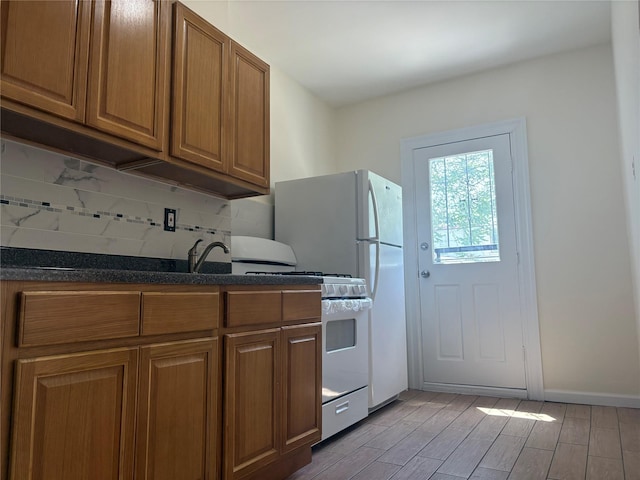 262 Grant Ave, Brooklyn, NY 11208 - kitchen featuring white gas range oven, brown cabinetry, decorative backsplash, light wood-type flooring, and dark stone countertops