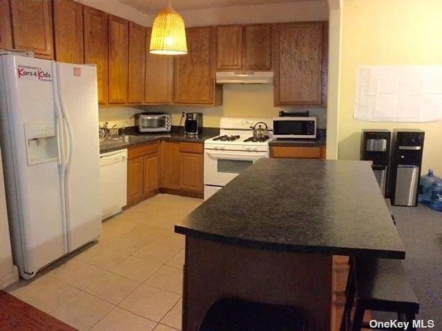 205 Aquatic Pl, Arverne, NY 11692 - kitchen featuring white appliances, under cabinet range hood, dark countertops, and decorative light fixtures
