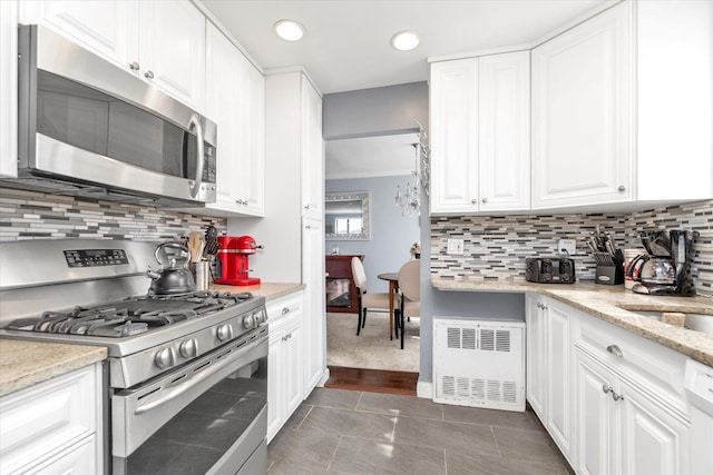 333 E Broadway Unit 1D, Long Beach, NY 11561 - kitchen with stainless steel appliances, radiator heating unit, white cabinets, decorative backsplash, and recessed lighting