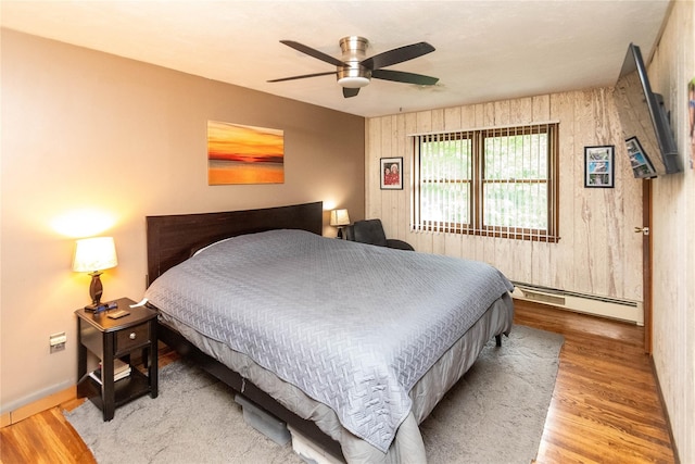26 Stacey Dr, Monticello, NY 12701 - bedroom with a baseboard heating unit, wooden walls, wood finished floors, a ceiling fan, and baseboards