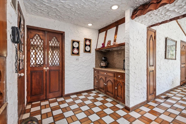 foyer featuring a textured wall, light floors, and baseboards