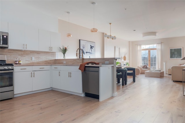 249 Main St Unit 401, Beacon, NY 12508 - kitchen featuring appliances with stainless steel finishes, open floor plan, decorative backsplash, light wood-style floors, and a peninsula