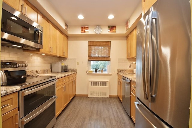 95 Charter Cir Unit 95, Ossining, NY 10562 - kitchen featuring appliances with stainless steel finishes, radiator, a sink, light wood-style flooring, and decorative backsplash