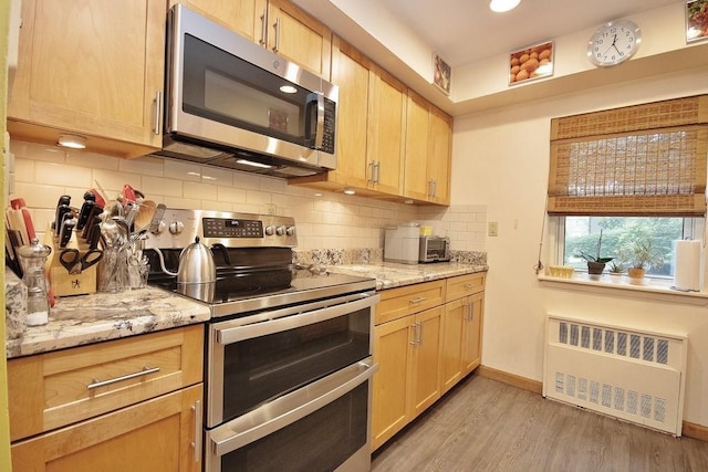 95 Charter Cir Unit 95, Ossining, NY 10562 - kitchen with appliances with stainless steel finishes, radiator heating unit, light wood-style flooring, decorative backsplash, and light stone counters