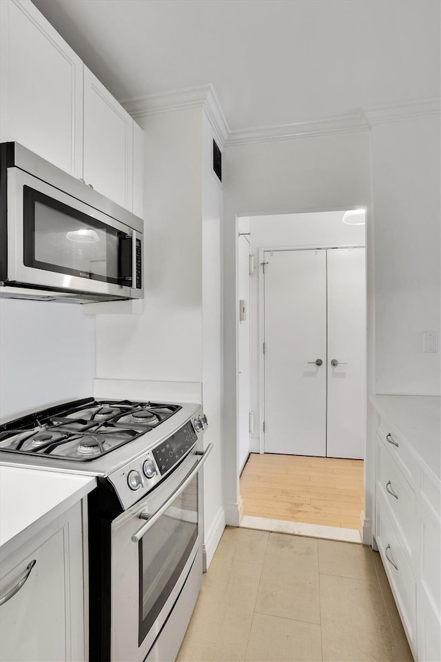 211 E 46th St Unit 14E, New York Manhattan, NY 10017 - kitchen with appliances with stainless steel finishes, ornamental molding, white cabinets, and light countertops