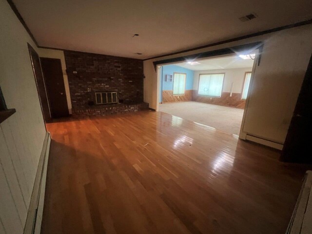 420 S Plank Rd, Westtown, NY 10998 - unfurnished living room with wood finished floors, a baseboard radiator, a brick fireplace, a wainscoted wall, and wood walls