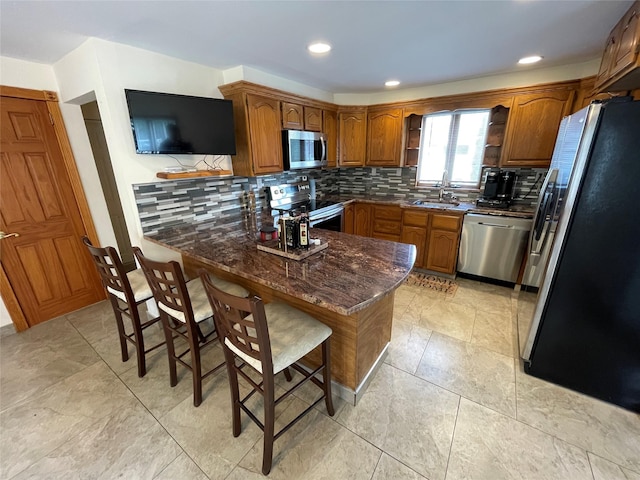 74 Webster Ave, West Islip, NY 11795 - kitchen featuring stainless steel appliances, brown cabinetry, decorative backsplash, dark stone countertops, and a breakfast bar