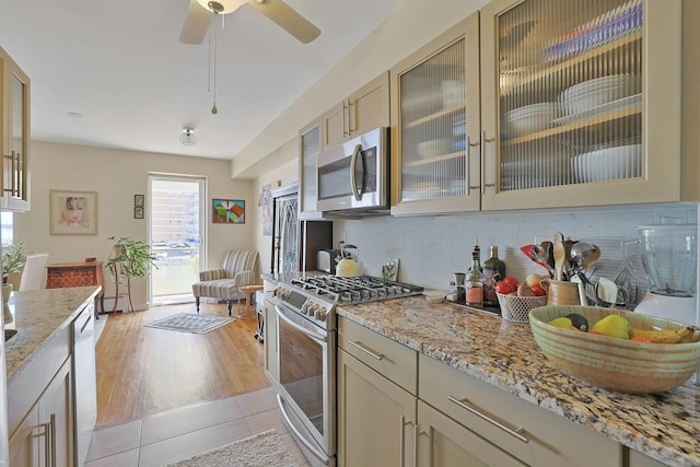 103 Gedney St Unit 2N, Nyack, NY 10960 - kitchen featuring stainless steel appliances, decorative backsplash, glass insert cabinets, light stone counters, and light tile patterned floors