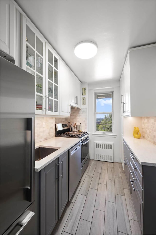 3135 Johnson Ave Unit 9A, Bronx, NY 10463 - kitchen with radiator heating unit, stainless steel appliances, wood finish floors, white cabinetry, and decorative backsplash