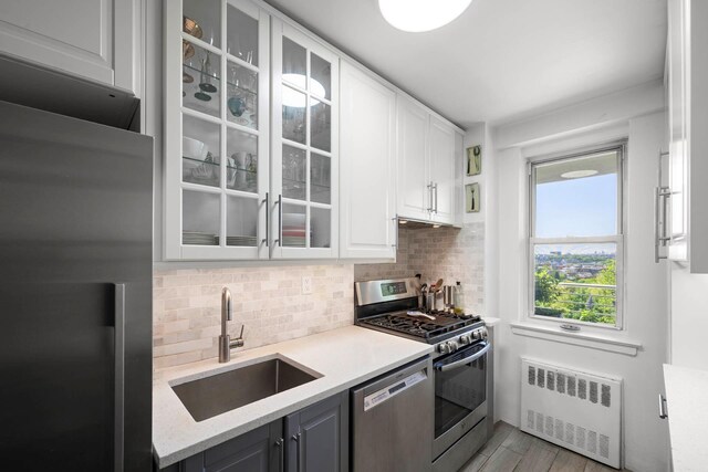 3135 Johnson Ave Unit 9A, Bronx, NY 10463 - kitchen featuring radiator, a sink, stainless steel appliances, decorative backsplash, and white cabinetry