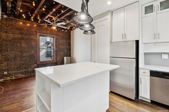 21-16 35th St Unit 5B, Astoria, NY 11105 - kitchen featuring appliances with stainless steel finishes, radiator heating unit, wood finished floors, brick wall, and a center island