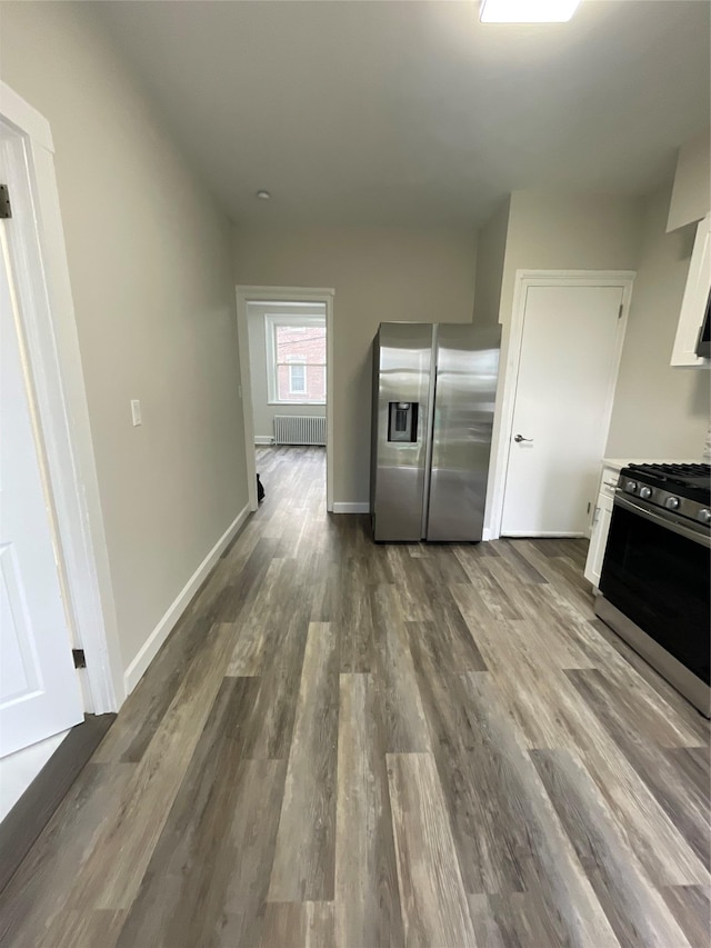 32 Moquette Row S, Yonkers, NY 10703 - kitchen featuring appliances with stainless steel finishes, radiator heating unit, white cabinets, dark wood-style flooring, and baseboards