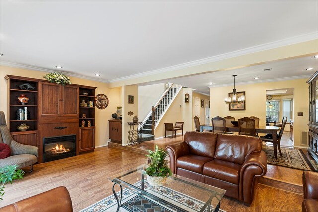 38 The Mews, Syosset, NY 11791 - living room featuring stairway, a glass covered fireplace, light wood finished floors, ornamental molding, and a chandelier