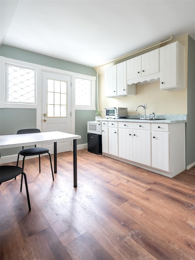 511 Grand Ave, Newburgh, NY 12550 - kitchen with white microwave, light wood-style flooring, light countertops, a sink, and white cabinetry