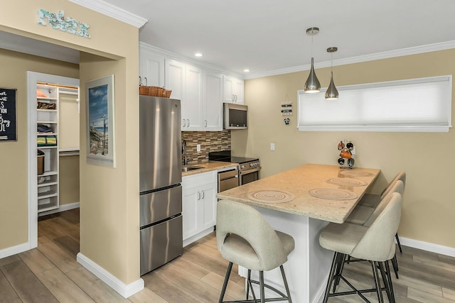 281 Dune Rd Unit 18A, Westhampton Beach, NY 11978 - kitchen with stainless steel appliances, a breakfast bar area, white cabinetry, light wood finished floors, and crown molding