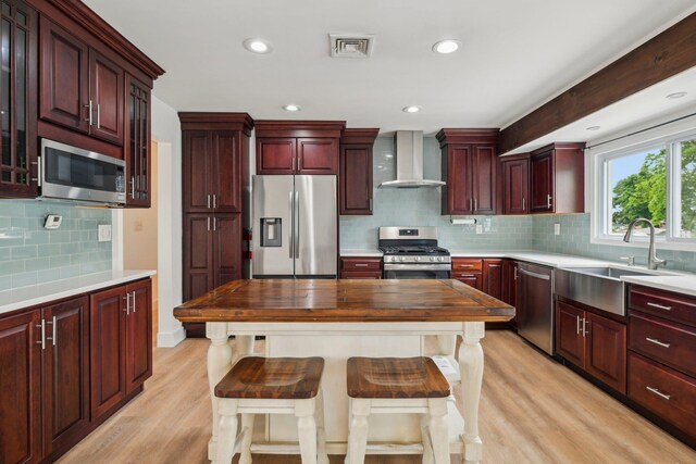 872 Main St, Farmingdale, NY 11735 - kitchen with wall chimney exhaust hood, appliances with stainless steel finishes, a sink, reddish brown cabinets, and light wood-style flooring