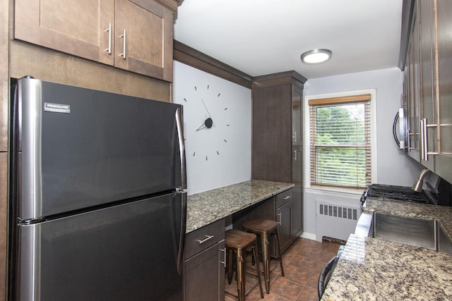 251-10 71st Rd Unit 30A, Bellerose, NY 11426 - kitchen with stainless steel appliances, radiator heating unit, light stone counters, dark tile patterned flooring, and dark brown cabinets