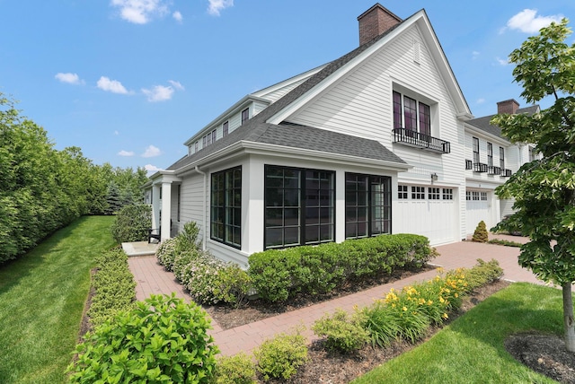 27 Lavender Ln, Rye Brook, NY 10573 - view of side of property featuring a shingled roof, a garage, a balcony, a chimney, and driveway