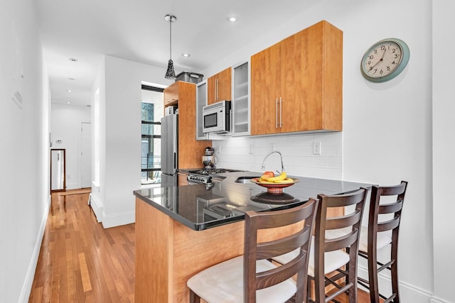 161 W 133rd St, New York Manhattan, NY 10030 - kitchen featuring brown cabinetry, white microwave, tasteful backsplash, baseboards, and light wood-style floors