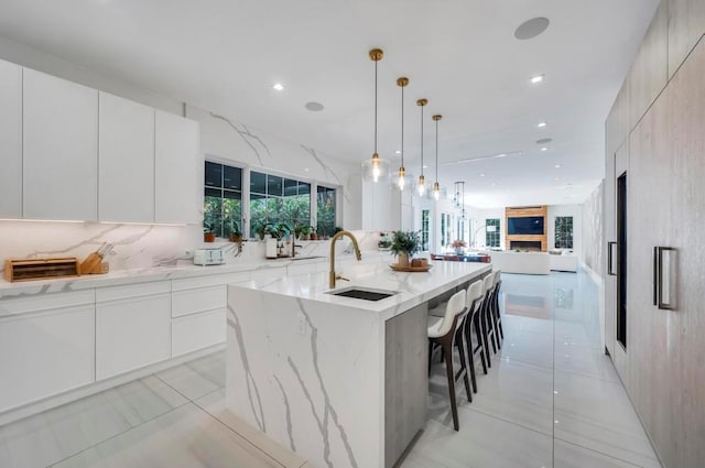 50 Gristmill Ln, Great Neck, NY 11023 - kitchen with a sink, modern cabinets, open floor plan, light stone counters, and a kitchen island with sink