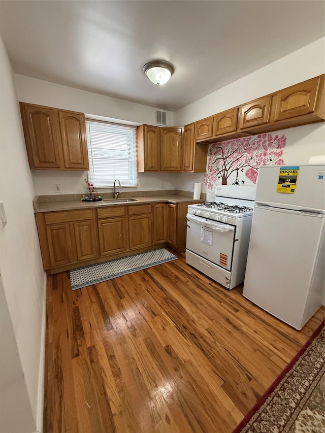 10808 86th St, Ozone Park, NY 11417 - kitchen with white appliances, light wood finished floors, a sink, and brown cabinetry
