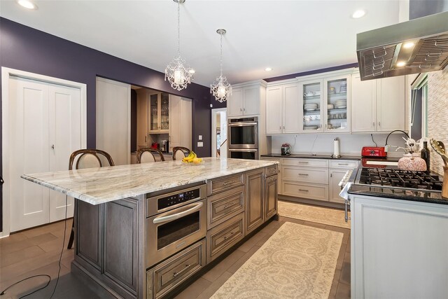 96 Cherry Hill Ct, Briarcliff Manor, NY 10510 - kitchen with wall chimney range hood, appliances with stainless steel finishes, a breakfast bar area, white cabinets, and a center island