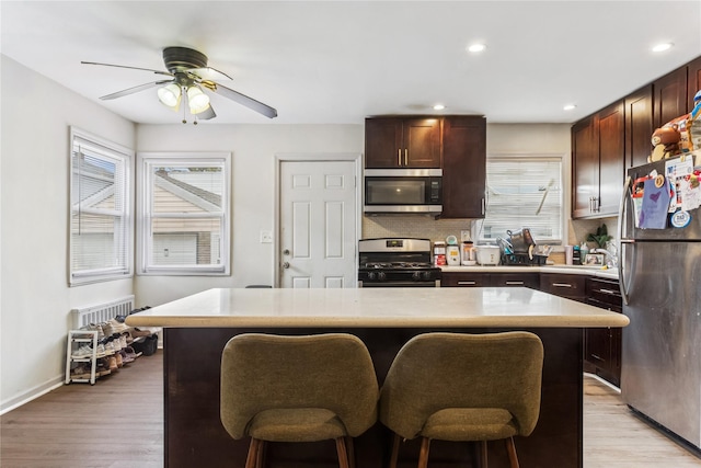 1343 E St, Elmont, NY 11003 - kitchen featuring appliances with stainless steel finishes, light countertops, a breakfast bar, light wood-type flooring, and backsplash
