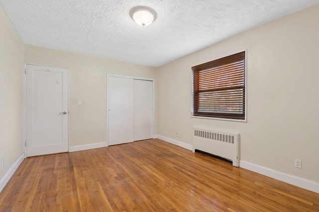 199-07 21st Ave Unit 1-361, Whitestone, NY 11357 - unfurnished bedroom featuring radiator, wood finished floors, baseboards, a textured ceiling, and a closet