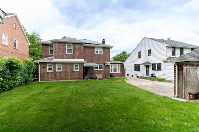 42-32 204th St, Bayside, NY 11361 - rear view of property with brick siding, roof mounted solar panels, a lawn, and a chimney