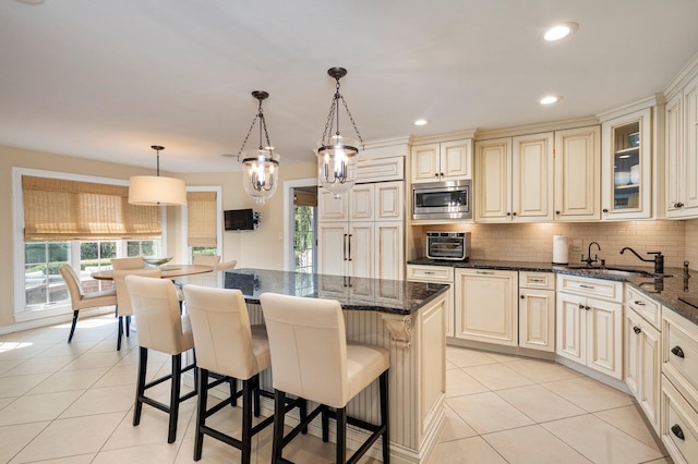 82 Woods Dr, East Hills, NY 11576 - kitchen featuring cream cabinets, stainless steel microwave, a sink, light tile patterned flooring, and decorative backsplash