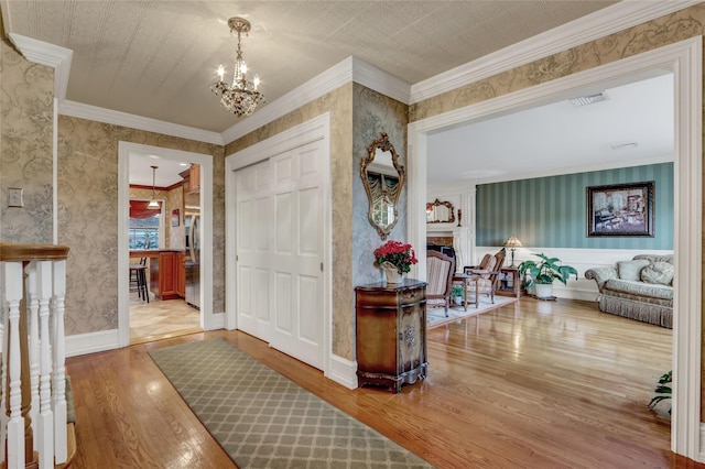 100 Fairfax Rd, Massapequa, NY 11758 - foyer featuring wood finished floors, a chandelier, wallpapered walls, a fireplace, and ornamental molding
