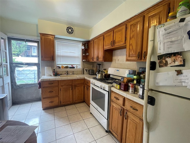 1037 E 214th St, Bronx, NY 10469 - kitchen with white appliances, tile countertops, brown cabinets, tasteful backsplash, and healthy amount of natural light